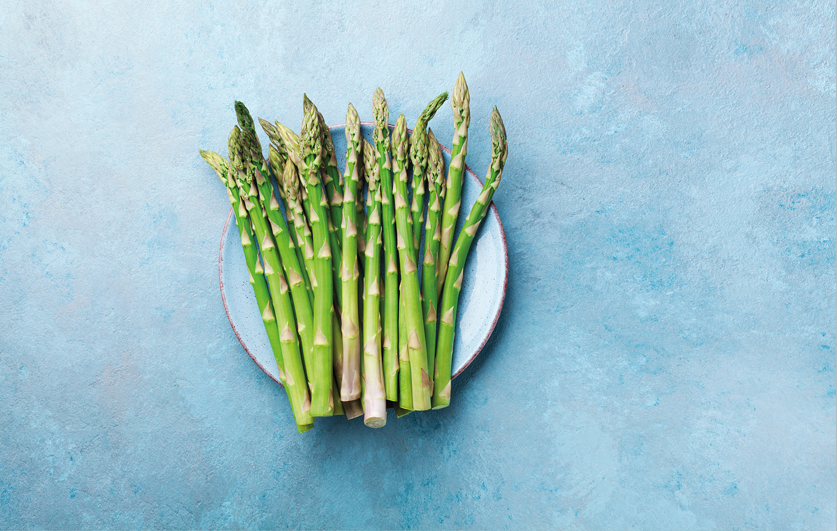 Fresh green asparagus in a blue bowl, top view.